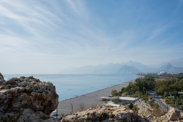 view from the hill to the city, high mountains covered with haze and clouds, surrounded by a blue sea that goes beyond the horizon