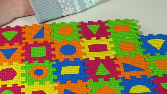 The child plays with soft multi-colored puzzles. Soft mat in the form of pieces of the puzzle. Top view. First peson view from above.