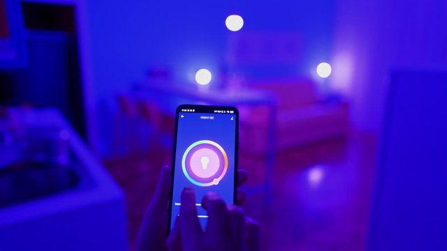 Woman changing color of the lights with smart home app on her smartphone. Smart home house concept. 4K