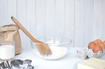 ingredients for home baking are laid out on the table: flour in a glass bowl, butter, sugar, eggs, cookie molds. Preparing to cook a pie in a bright kitchen