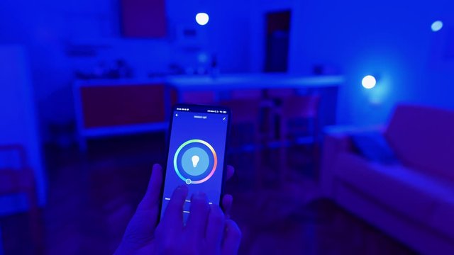 Smart home house lightning concept. Woman hands and smartphone. Controlling color of light bulbs in room via Smart Home Application