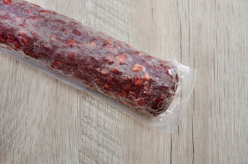 Sausage in plastic vacuum package on wooden background.