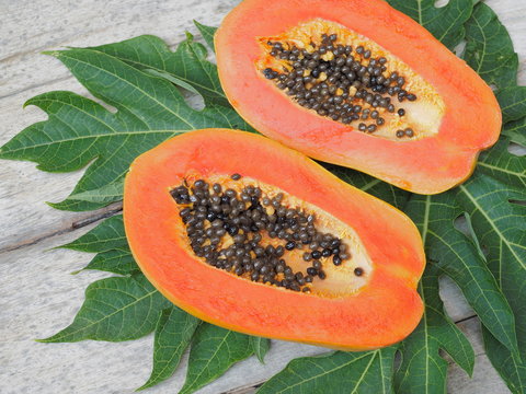 Top view of ripe Papaya and seeds on green papaya leaves and wood texture background.