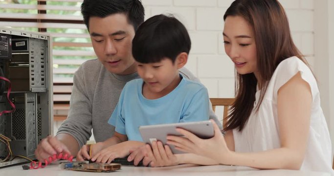 Young mother and father assist they son to assembling a computer at home. Mother open information in tablet to help little boy. Technology, Education, Family and Innovation concept.