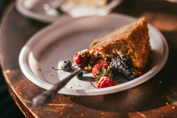 A piece of homemade blueberry and raspberry pie lies on a plastic white plate with silver spoon against the backdrop of a wooden table. Selective focus macro shot with shallow DOF