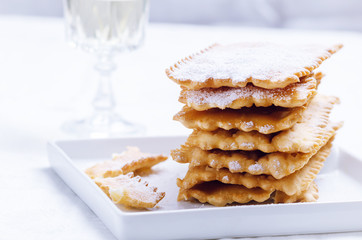 Italian frappe or chiacchiere  - typical  carnival fritters dusted with powdered sugar on  white plate.
