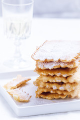 Italian frappe or chiacchiere  - typical  carnival fritters dusted with powdered sugar on  white plate.