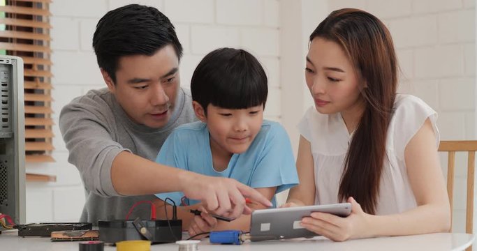 Young mother and father assist they son to assembling a computer at home. Mother open information in tablet to help little boy. Technology, Education, Family and Innovation concept.