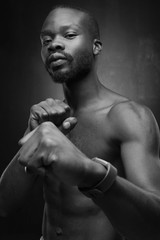 black and white portrait of a black handsome guy with a naked torso who holds his fists in front of him with watch on his arm
