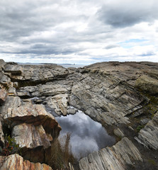 Fototapeta na wymiar Rocky cliff shore with a puddle of sky reflection and a lighthouse in the distance in the ocean. Vertical panorama. The coast of the Atlantic Ocean. USA. Portland Maine