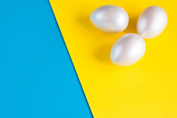 Easter holiday composition. Three eggs of silver color on a double yellow-blue background. Easter flat ley. Easter concept. Copyspace.