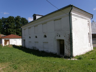 An old brick building painted white with fully enclosed Windows with a blue sky and green grass