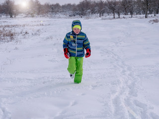 Fototapeta na wymiar funny children in bright winter jackets and trousers walk in snowy field near village. boys lie on snow, jump, somersault, waving their hands depicting snow angels