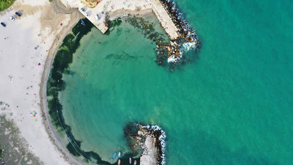 Aerial top down view of Bolata Cove on Black sea, Bulgaria. White sand beach on the sea shore near cape Kaliakra. Stones, foaming waves, sunbathing people and colorful boats from above.