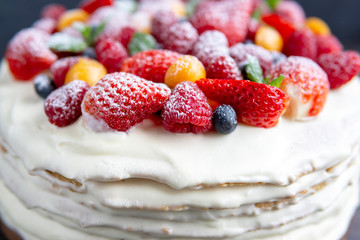 Homemade white cream cake with fresh berries on rustic wooden table, dark background with copy space. Beautiful, tasty dessert made of natural products. Selective focus. Holiday, birthday food concept
