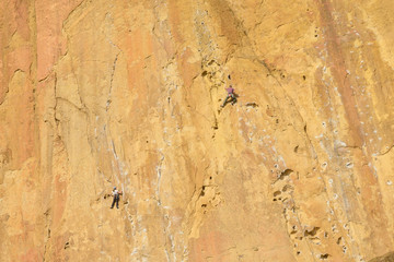 Climbers climb a large rock, filmed from the back. With space