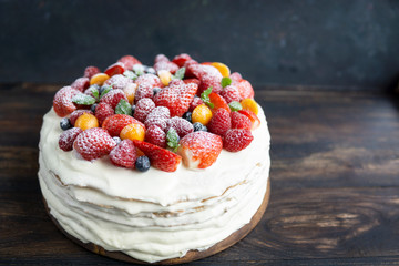 Homemade white cream cake with fresh berries on rustic wooden table, dark background with copy space. Beautiful, tasty dessert made of natural products. Selective focus. Holiday, birthday food concept