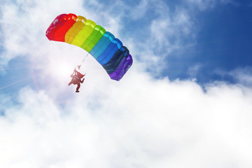 Skydiver flying on a parachute rainbow colors in the sun, against the sky.