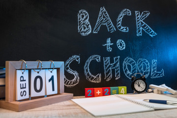 Still life with clock, writing materials, a book and an apple against blackboard with text "back to school"