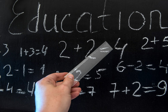 Teacher writing various primary school maths formula on chalkboard.