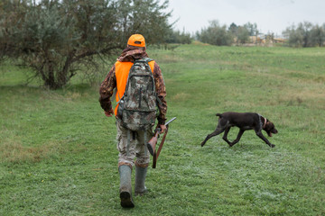 A man with a gun in his hands and an orange vest on a pheasant hunt in a wooded area in cloudy...