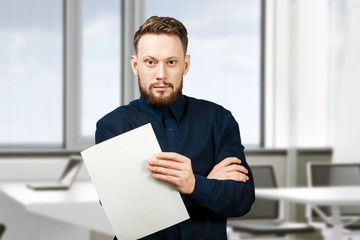 man holding blank sheet of paper. Young guy pointing at paper sheet and looking at camera. Promotion concept.