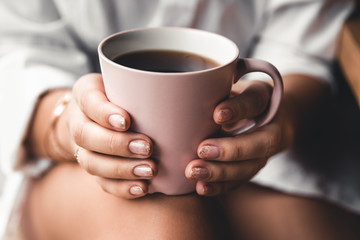 Woman in a white t-shirt holds morning coffee in a pink ceramic cup. Manicure. Front view