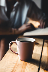 Beautiful woman in the morning drinks coffee and reads old book in a white shirt. Education, drink.