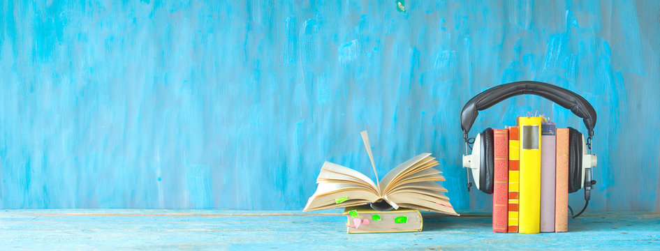 audio book concept with open book, row of books and headphones, panorama format on grungy background, good copy space