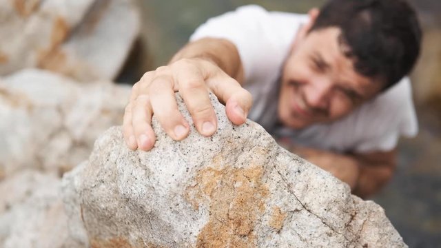 A climber man, having reached the summit, does everything possible, climbs up. Close up on a hand.