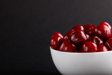 Fresh red sweet cherry in white bowl on black background. side view.