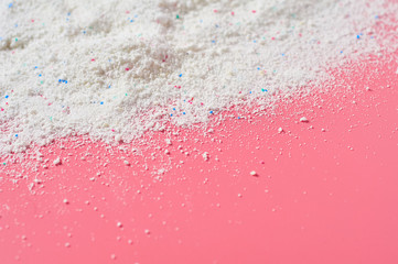 Scattered heap of washing powder for cleaning clothes lies on pink countertop in laundry. Space for text