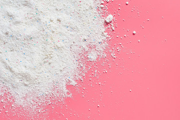 Scattered heap of washing powder for cleaning clothes lies on pink countertop in laundry. Space for...