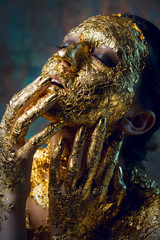 Girl with a mask on her face made of gold leaf. Gloomy studio portrait of a brunette on an abstract background.