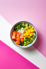 Hawaiian salmon poke bowl with seaweed, avocado, edamame, mango and pickled ginger. Top view, bright pink background