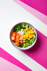 Hawaiian salmon poke bowl with seaweed, avocado, edamame, mango and pickled ginger. Top view, bright pink background