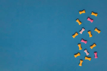 Multicolor sweets in the form of a dog bone on a blue background. Flat lay, copy space, top view.