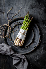 Bunch of fresh green asparagus on vintage metal tray over dark grey rustic background. Top view,...