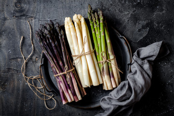 Bunches of fresh green, purple, white asparagus on vintage metal tray over dark grey rustic background. Top view, copy space - obrazy, fototapety, plakaty