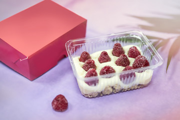 Delicious dessert in plastic package with raspberry on table and pink wrapping close up. Food concept