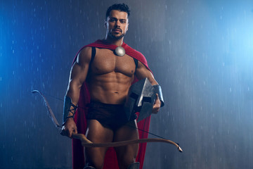 Muscular wet spartan archer holding helmet.