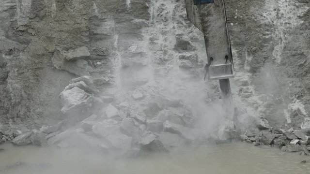Excavator with big hydraulic rock breaker demolishing limestone