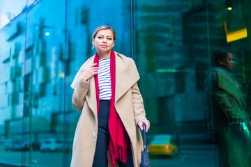 Obraz na płótnie Canvas Outdoors lifestyle fashion portrait of stunning brunette girl. Walking on the city street. Going shopping. Wearing stylish white fitted coat, red neckscarf, black umbrella cane. Business woman.