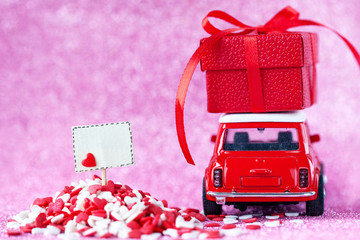 Back view. Red toy car delivering carrying on roof gift box and empty board on shiny pink background.
