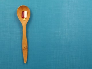 Top view photo of a wooden spoon on a blue surface, with three different pills in it. Taking vitamins/medicine concept.