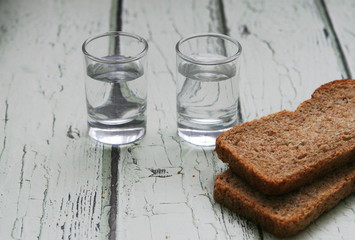 two glasses of vodka and pieces of black bread on a light wooden table