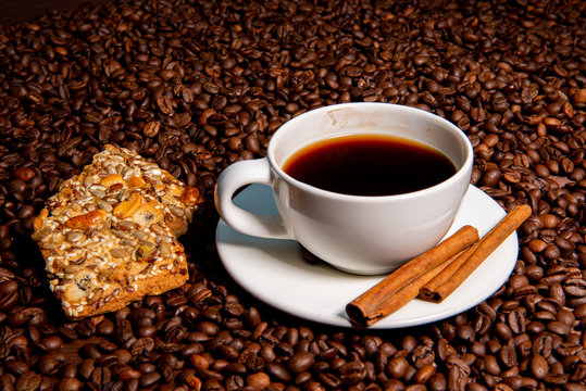 White coffee mug,  cinnamon sticks and cookies on the coffee beans background - image
