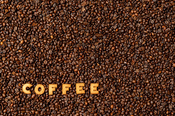 Obraz na płótnie Canvas The word COFFEE made from biscuit letters on a dark coffee bean background