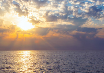 Natural tropical sundown on the sea with dramatic clouds. Sunset sky backlit by the sun over the ocean. Colorful rays reflected in the water. Travel background.