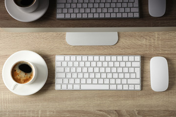 Computer, keyboard, cup of coffee and mouse on wooden background, top view